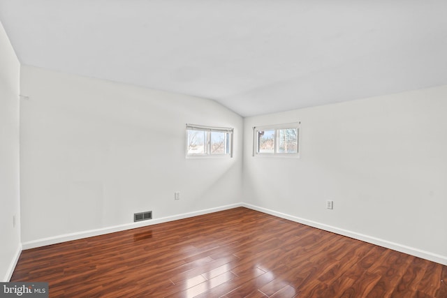 spare room with baseboards, visible vents, vaulted ceiling, and dark wood-style flooring