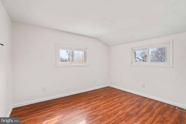 spare room with vaulted ceiling, visible vents, plenty of natural light, and wood finished floors