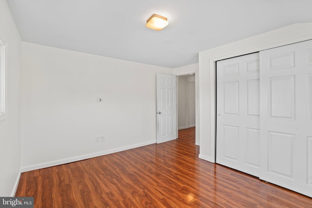 unfurnished bedroom with baseboards, dark wood finished floors, and a closet