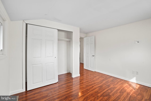 unfurnished bedroom with dark wood-style floors, baseboards, vaulted ceiling, and a closet