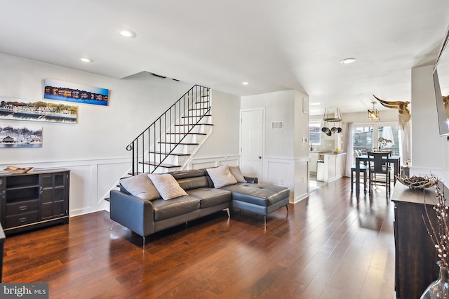 living area featuring dark wood-style flooring, visible vents, a decorative wall, stairway, and wainscoting