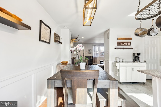 dining space featuring light tile patterned floors, a decorative wall, and wainscoting