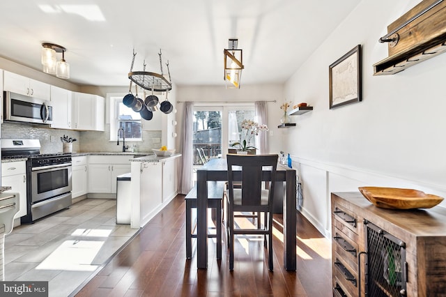 kitchen featuring a wainscoted wall, stainless steel appliances, decorative backsplash, white cabinets, and light wood-type flooring