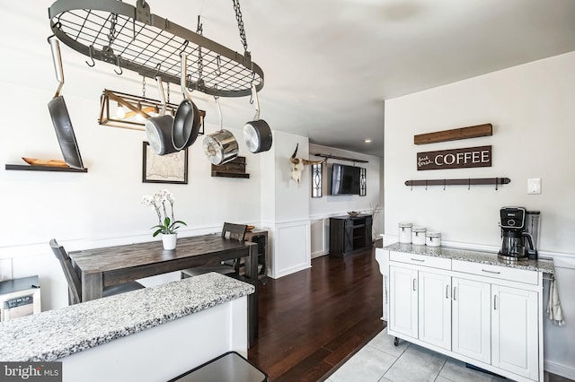 kitchen with light stone countertops, a wainscoted wall, and white cabinetry