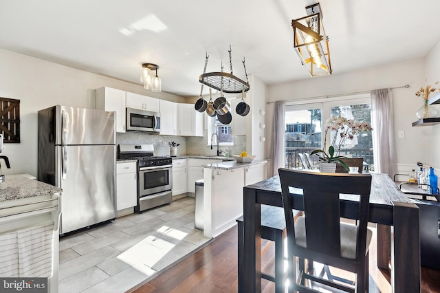 kitchen with light stone counters, stainless steel appliances, decorative backsplash, white cabinets, and a sink