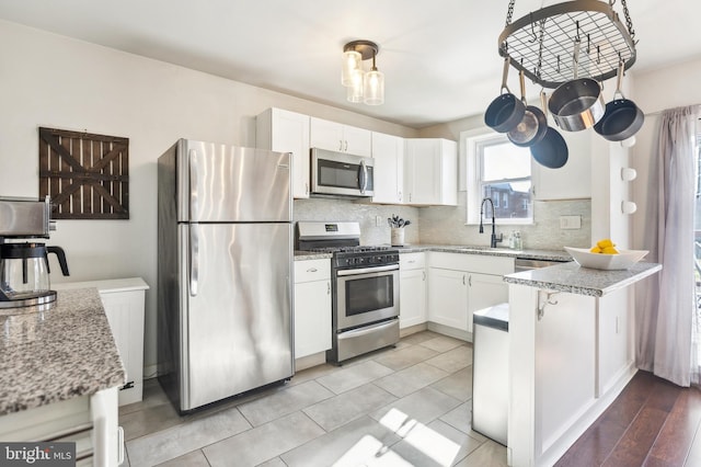 kitchen with tasteful backsplash, appliances with stainless steel finishes, a sink, and white cabinets