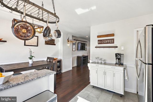 kitchen featuring freestanding refrigerator, wainscoting, a decorative wall, and light stone countertops