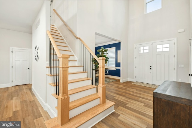 entrance foyer featuring light wood-style floors, baseboards, stairs, and a high ceiling