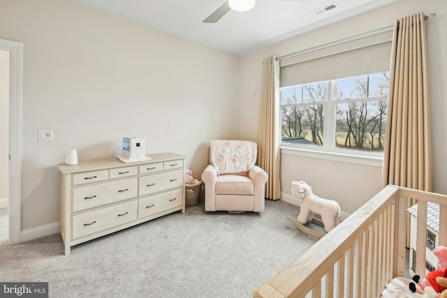 bedroom featuring light carpet, a crib, baseboards, visible vents, and ceiling fan