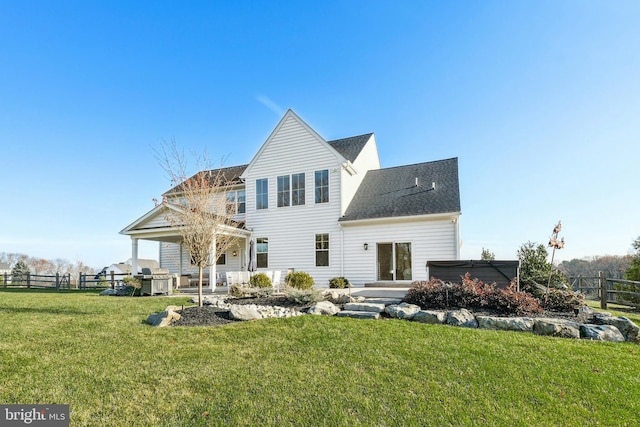 rear view of property with a hot tub, fence, and a yard