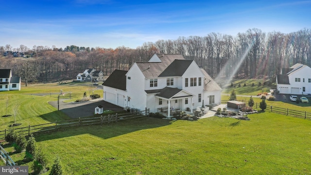 back of house featuring a garage, driveway, a lawn, a rural view, and fence