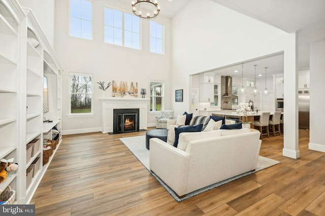 living area with a fireplace with flush hearth, light wood-type flooring, a notable chandelier, and baseboards