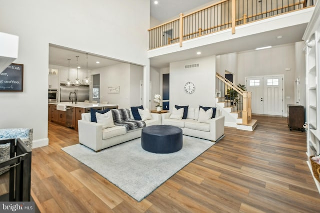 living room with visible vents, stairway, a towering ceiling, light wood-type flooring, and baseboards