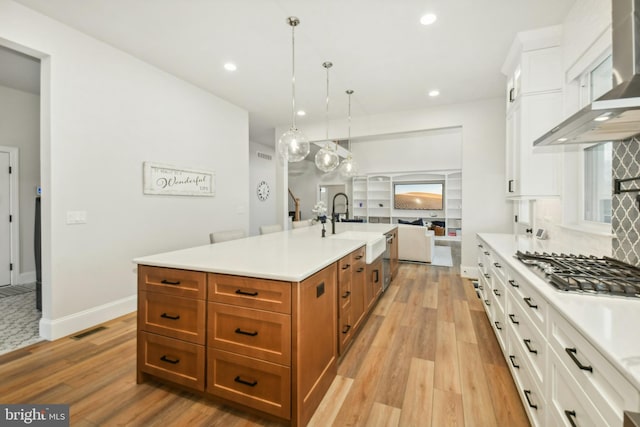 kitchen with a sink, hanging light fixtures, light countertops, a large island, and wall chimney exhaust hood