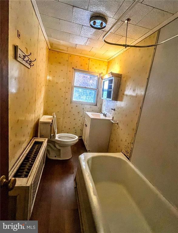 bathroom with toilet, wood finished floors, vanity, a tub, and crown molding