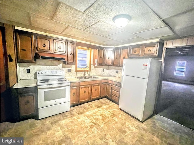 kitchen with white appliances, brown cabinets, light countertops, under cabinet range hood, and a sink