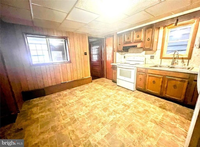 kitchen with white electric range oven, light countertops, wood walls, a sink, and under cabinet range hood