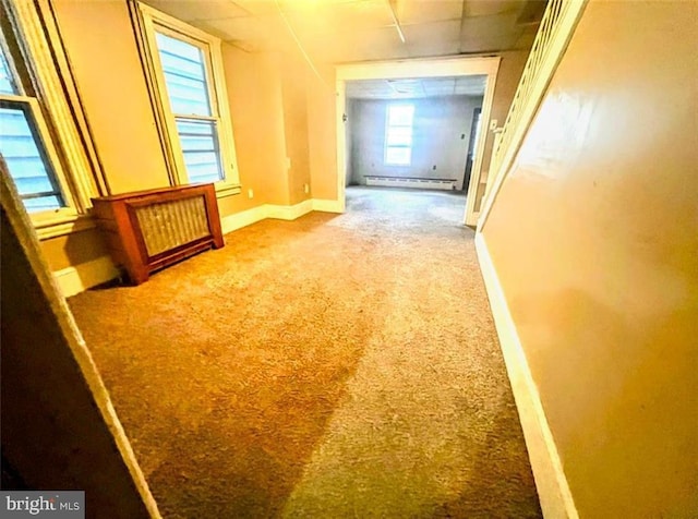 hall featuring carpet floors, baseboards, a baseboard heating unit, and a drop ceiling