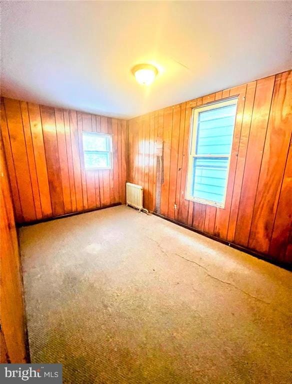 empty room featuring wood walls, light colored carpet, and radiator