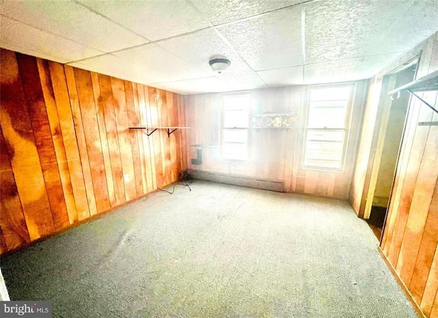 carpeted spare room featuring a drop ceiling and wooden walls