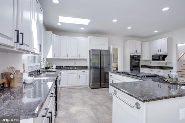 kitchen with a sink, a skylight, black appliances, and white cabinetry