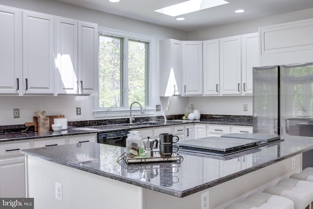 kitchen with a skylight, a center island, a sink, white cabinets, and dark stone countertops