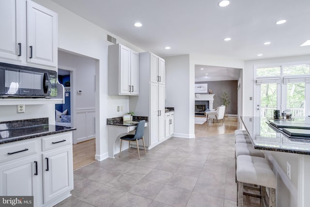 kitchen featuring black microwave, dark stone counters, a glass covered fireplace, and recessed lighting