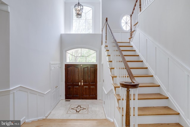 entrance foyer with a decorative wall, a high ceiling, stairway, a wainscoted wall, and a chandelier