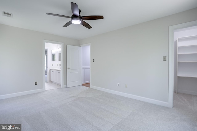 unfurnished bedroom with a walk in closet, baseboards, light carpet, and visible vents