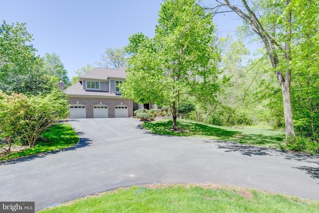 view of property hidden behind natural elements featuring a garage, driveway, and a chimney