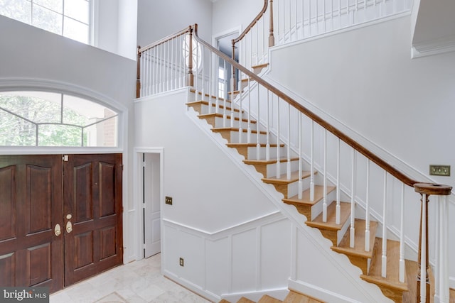 entrance foyer with a decorative wall, wainscoting, stairway, and a towering ceiling