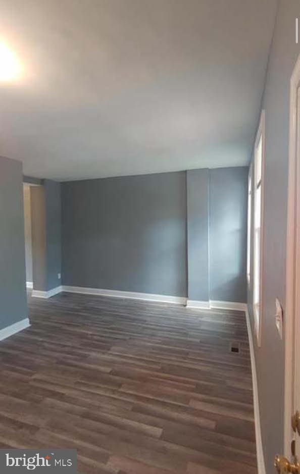 unfurnished room featuring dark wood-type flooring, visible vents, and baseboards