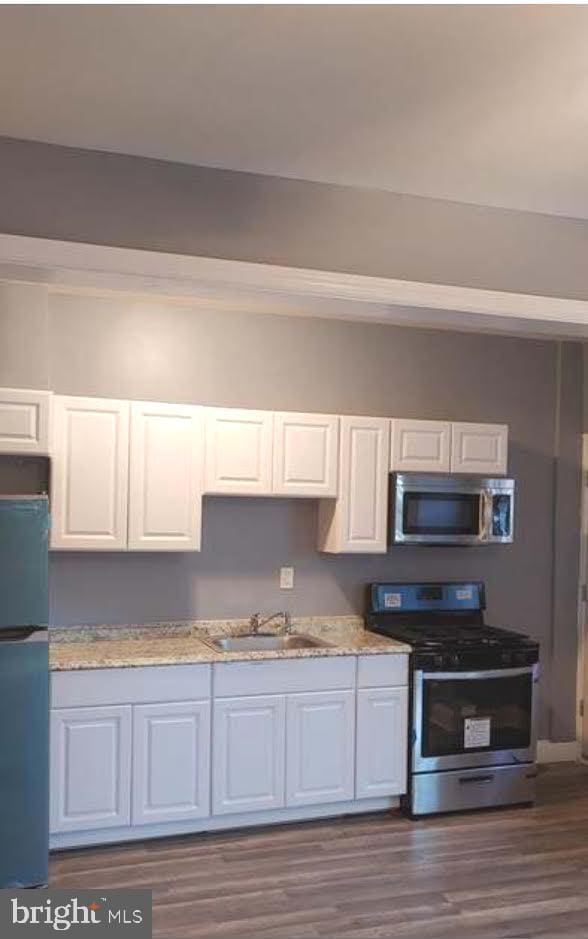 kitchen with light stone countertops, dark wood finished floors, a sink, white cabinets, and appliances with stainless steel finishes