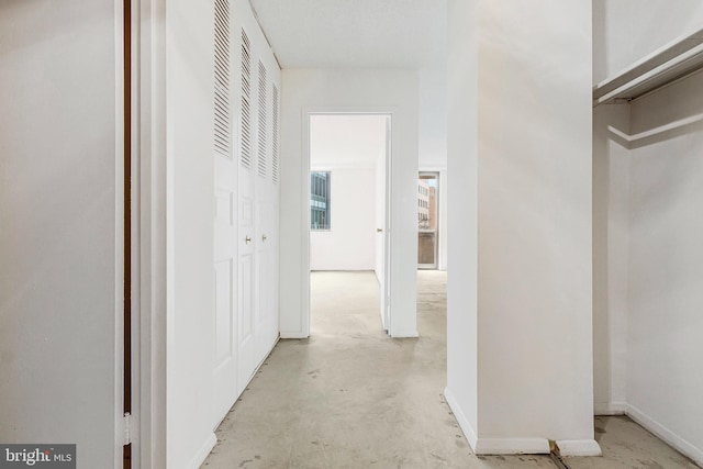 hall featuring unfinished concrete flooring and baseboards