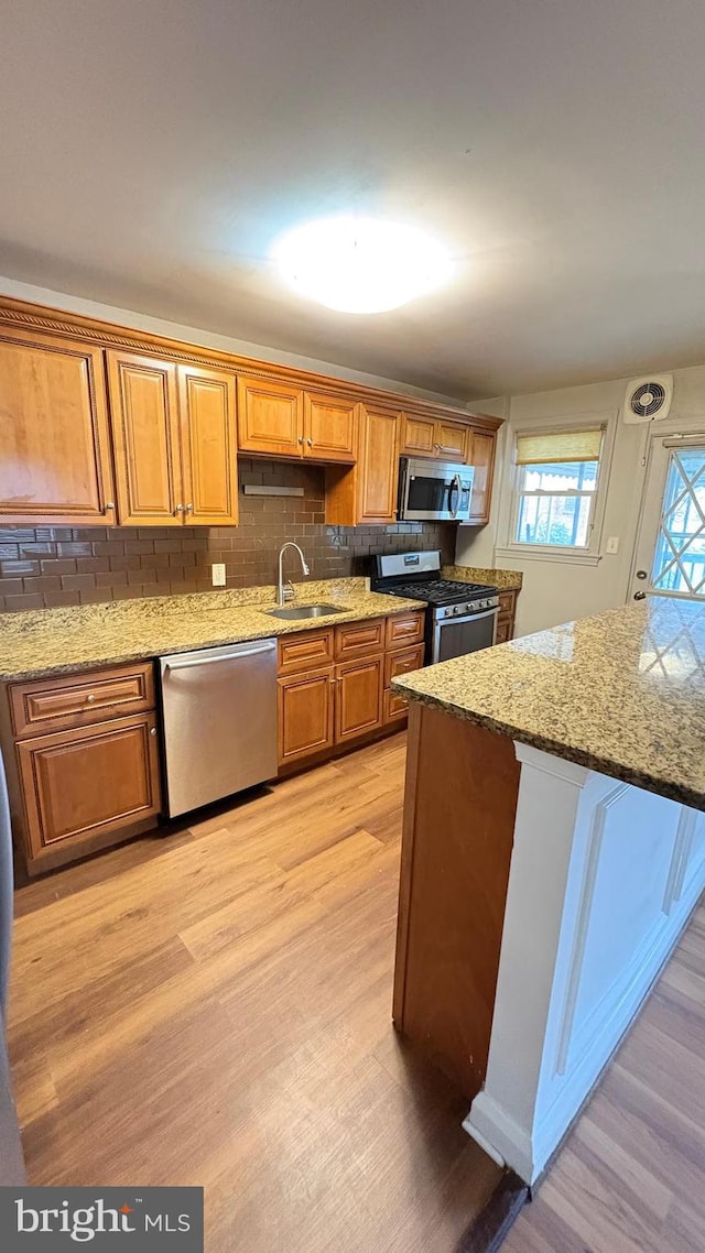 5716 Willowton Ave, Baltimore, MD 21239 - kitchen featuring light wood-style flooring, light stone counters, a sink, stainless steel appliances, and brown cabinets