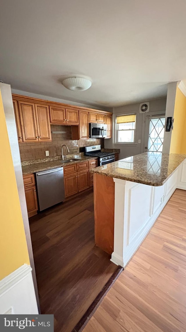 5716 Willowton Ave, Baltimore, MD 21239 - kitchen featuring dark wood-style flooring, a peninsula, brown cabinetry, appliances with stainless steel finishes, and a sink