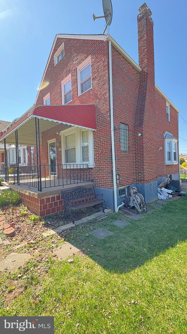 5716 Willowton Ave, Baltimore, MD 21239 - view of side of home with brick siding, a chimney, a lawn, and covered porch