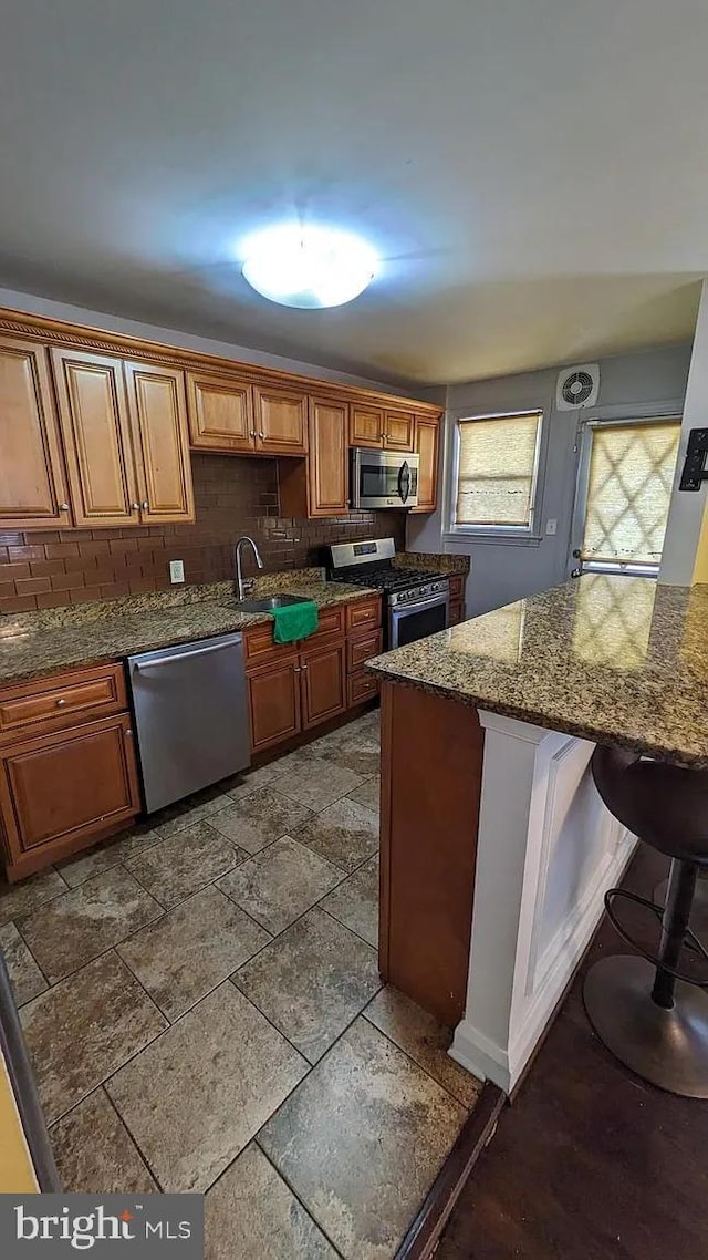 5716 Willowton Ave, Baltimore, MD 21239 - kitchen with a sink, brown cabinets, dark stone counters, stainless steel appliances, and a breakfast bar area