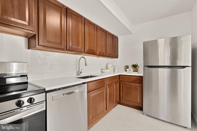 kitchen featuring stainless steel appliances, a sink, light countertops, and brown cabinets