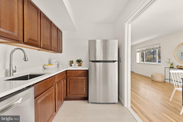 kitchen featuring dishwasher, a sink, freestanding refrigerator, and brown cabinets