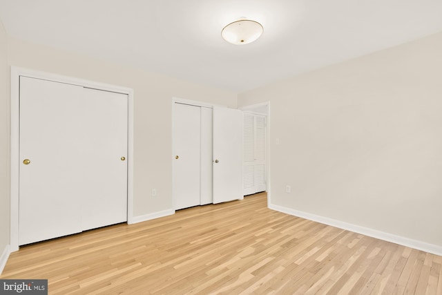 unfurnished bedroom with light wood-style floors, baseboards, and multiple closets