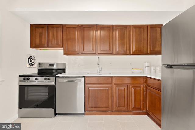 kitchen with brown cabinetry, stainless steel appliances, a sink, and light countertops