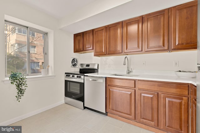 kitchen with a sink, baseboards, light countertops, appliances with stainless steel finishes, and brown cabinetry