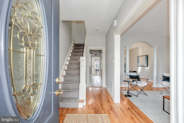 entrance foyer with arched walkways, light wood-style floors, stairs, and ornate columns