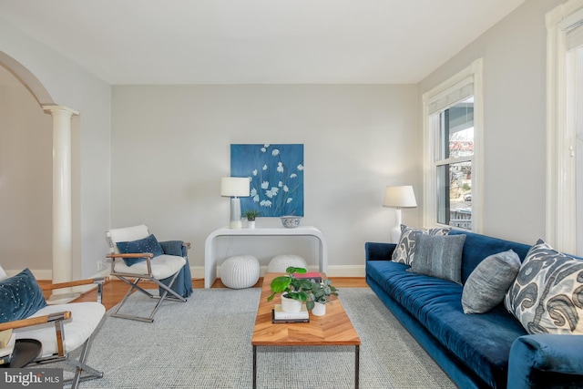 living area featuring arched walkways, wood finished floors, decorative columns, and baseboards