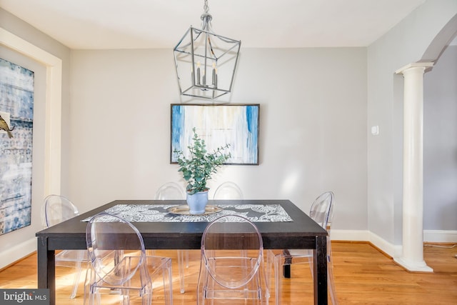 dining area featuring arched walkways, ornate columns, a chandelier, light wood-type flooring, and baseboards