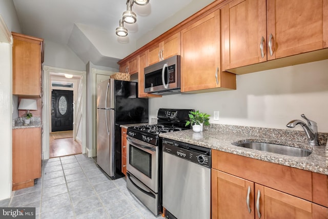 kitchen with brown cabinetry, light stone countertops, vaulted ceiling, stainless steel appliances, and a sink