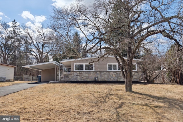 view of front of home with fence, stone siding, driveway, a carport, and a front lawn