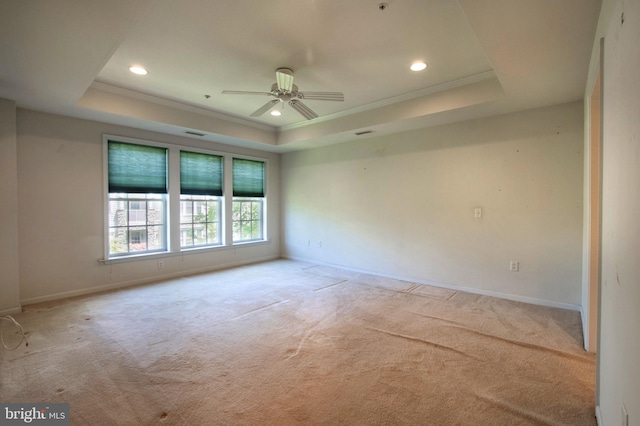 empty room with ornamental molding, a tray ceiling, light colored carpet, and baseboards