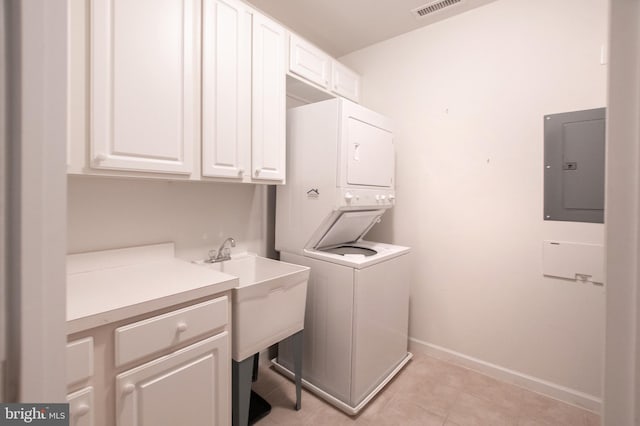 laundry area featuring cabinet space, electric panel, baseboards, stacked washer and clothes dryer, and light tile patterned flooring